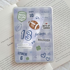 Puede incluir: Funda transparente para teléfono con un diseño de cuadros azules y blancos, adornada con varias pegatinas. Incluyen un balón de rugby, el número 13 y frases como "for keeps" y "Nice legs".