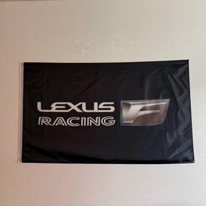 May include: Black flag with the words "LEXUS RACING" in white, along with the Lexus logo in silver. The flag is rectangular and hangs on a wall.