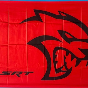 May include: A red flag with a large black graphic of a snarling beast's head. The letters "SRT" are printed in black at the bottom. The flag has a white border on the left side.