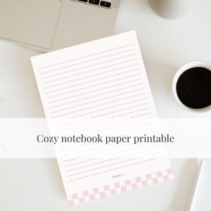 Może przedstawiać: Biała, liniowana kartka papieru do notatnika z napisem "Cozy notebook paper printable". Dolna krawędź ma różowo-biały wzór w szachownicę. Widoczny jest również laptop, filiżanka kawy i długopis.