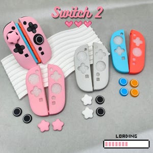 Könnte beinhalten: Switch 2 Controller-Zubehör in Rosa, Grau, Blau und Orange. Das Bild zeigt Controller-Schalen, Daumengriffe und Knöpfe. Der Text "Switch 2" ist oben abgebildet, mit einer Ladebalken-Grafik unten.