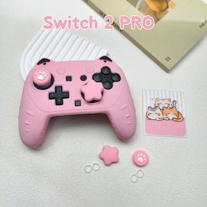 Peut inclure: Manette rose Switch 2 Pro avec boutons noirs et motif empreinte de patte. Comprend un bouton en forme d'étoile, un bouton empreinte de patte et un autocollant de chat. Le texte "Switch 2 PRO" est affiché en rose.