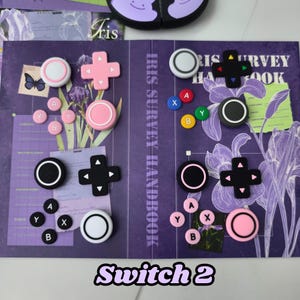 Puede incluir: Un conjunto de accesorios para el controlador Switch 2 en varios colores, incluyendo rosa, blanco, negro y amarillo. Los elementos están dispuestos sobre un fondo morado con motivos florales y texto. El texto "Switch 2" es visible.
