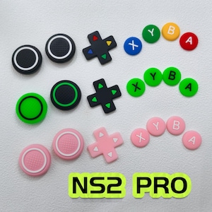 May include: A collection of colorful controller buttons and directional pads. The buttons are in various colors, including black, green, pink, blue, yellow, and red. The text "NS2 PRO" is displayed in a neon green rectangle.