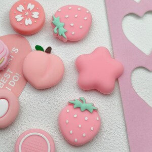 Pastel pink Nintendo Switch 2 joystick covers with strawberry and star aesthetic accessory set.