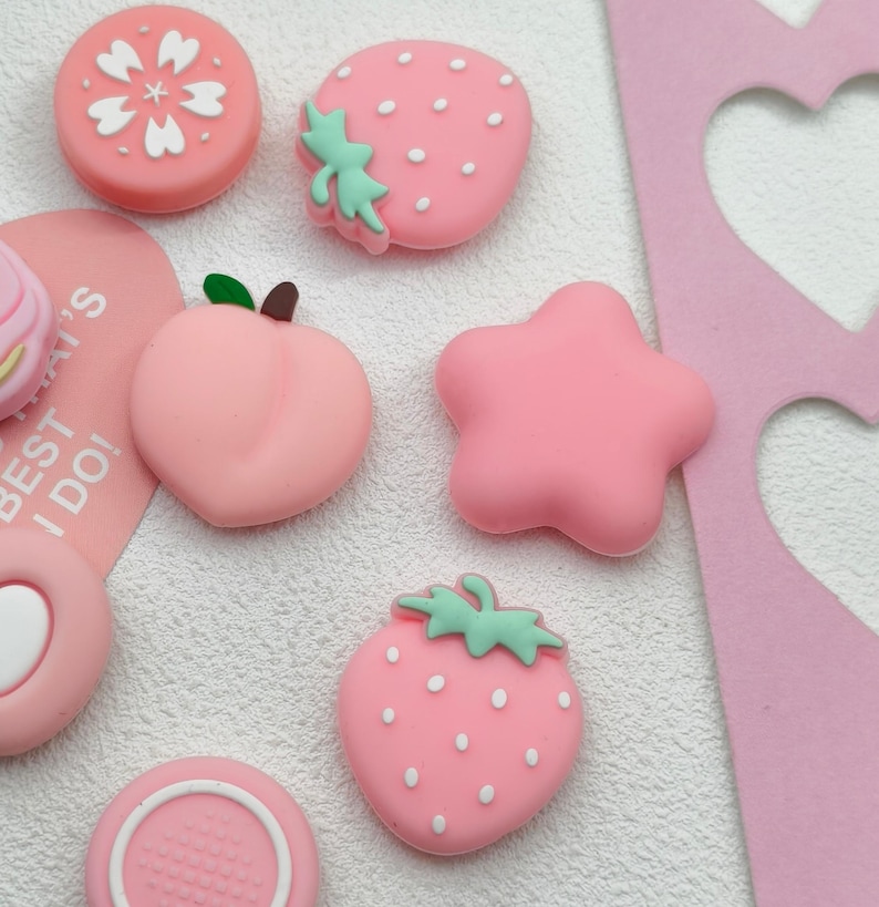 Pastel pink Nintendo Switch 2 joystick covers with strawberry and star aesthetic accessory set.