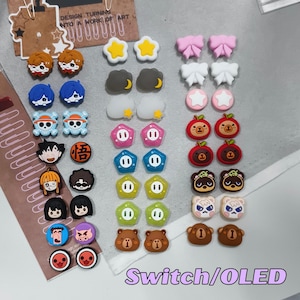 May include: A selection of colourful decorative charms in various shapes and designs. The charms include stars, bows, clouds, and cartoon characters. The text "Switch/OLED" is visible at the bottom of the image.