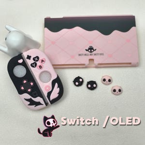May include: Pink and black Switch / OLED accessories set. Includes a pink and black controller cover, a pink case with a dark brown top, and black and pink thumb grips. The case has the text "Sweety Angel and Sweety Devil".