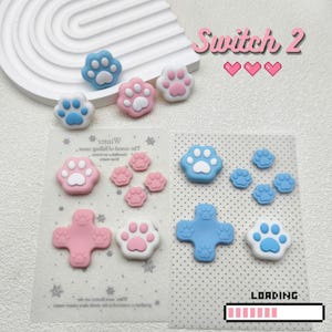 Può includere: Grip per pollice per controller a forma di zampe, blu, rosa e bianchi. L'immagine include il testo "Switch 2" e una barra di caricamento. Accessori per console di gioco.