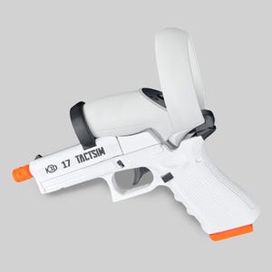 Puede incluir: Pistola blanca K3D 17 TACTSIM con punta naranja y correa negra. Un mando de realidad virtual blanco está sujeto a la parte superior de la pistola. La empuñadura de la pistola tiene un patrón texturizado.
