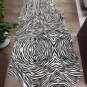 May include: A large, irregularly shaped animal hide rug featuring a bold, high-contrast black and white zebra stripe pattern. The hide displays a symmetrical, organic arrangement of stripes that flow across the surface in a continuous, repeating design.