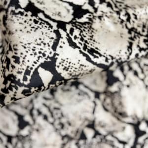 Könnte beinhalten: Nahaufnahme eines Stoffes mit Schlangenmuster. Der Stoff ist eine Mischung aus Schwarz und Off-White, wobei das Muster den Schuppen einer Schlange ähnelt. Der Stoff ist gefaltet und zeigt die Textur und die Details des Designs.
