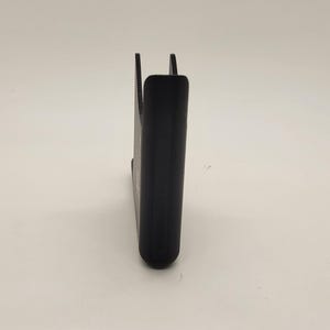 以下が含まれることがあります： 湾曲したデザインの黒いプラスチック製の携帯電話スタンド。スタンドは携帯電話を垂直に保持するように設計されています。