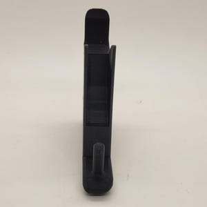以下が含まれることがあります： 下部にフックが付いた黒いプラスチック製の携帯電話スタンド。スタンドは携帯電話を垂直に保持するように設計されています。