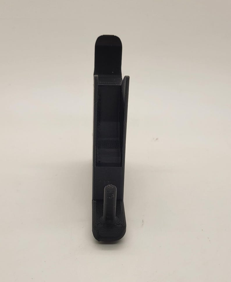 以下が含まれることがあります： 下部にフックが付いた黒いプラスチック製の携帯電話スタンド。スタンドは携帯電話を垂直に保持するように設計されています。