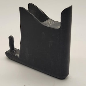 以下が含まれることがあります： 側面に小さなピンが付いた黒いプラスチック部品。部品は、湾曲した上部と平らな底部を持つユニークな形状をしています。背景には「5 YEARS IN-SERVICE」というテキストが表示されています。