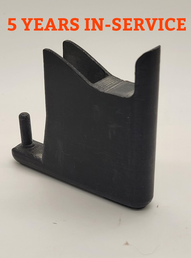 以下が含まれることがあります： 側面に小さなピンが付いた黒いプラスチック部品。部品は、湾曲した上部と平らな底部を持つユニークな形状をしています。背景には「5 YEARS IN-SERVICE」というテキストが表示されています。
