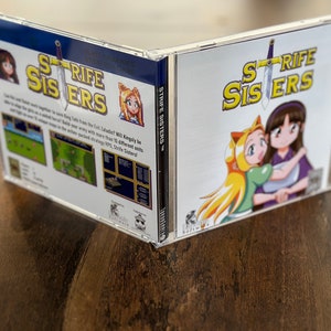 以下が含まれることがあります： 「Strife Sisters」というゲームの透明なプラスチックCDケース。表紙には、金髪で猫耳のカチューシャをした女の子と、黒髪の女の子の2人のアニメスタイルの女の子が描かれています。ゲームタイトルは黄色で、剣のグラフィックが付いています。