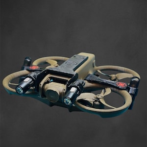 Op de afbeelding: Een bruin en zwarte drone met vier propellers en twee lampen. De drone heeft een camera en een getextureerde bovenkant. De propellers zijn lichtbruin van kleur en de behuizing is donkerder bruin. De achtergrond is donkergrijs.