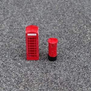 Puede incluir: Una cabina telefónica roja en miniatura y un buzón rojo en miniatura sobre una superficie gris.