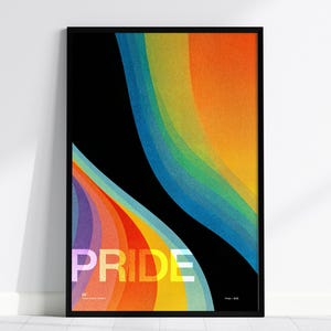 May include: A framed art print with a black border. The artwork features a black background with colorful, curved, textured bands in shades of orange, yellow, blue, and purple. The word "PRIDE" is printed in large, white letters.