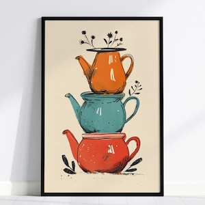 May include: A framed wall art print featuring a vertical stack of three teapots in orange, teal, and red. The top orange teapot contains black line-drawn flowers. The illustration uses a bold, graphic style with black outlines on a cream background.