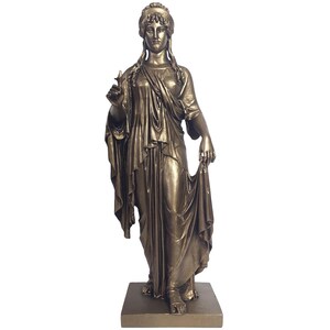 May include: A bronze-colored statue of a draped female figure, standing on a square base. The figure holds a small object in one hand and a fold of fabric in the other. The statue has detailed facial features and flowing garments.