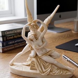 Può includere: Una scultura color crema raffigurante una coppia che si abbraccia, con una figura che ne tiene un'altra. La scultura ha ali dettagliate ed è posta su una base rettangolare. La scultura è su una scrivania di legno con libri e un computer sullo sfondo.