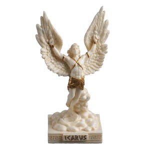 Peut inclure: Statue crème d'Icare avec des ailes et des bras tendus. La figurine a des accents dorés à la taille et aux poignets. La base de la statue porte le mot "ICARUS" en lettres dorées.