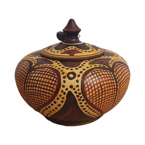 May include: A round, brown ceramic jar with a lid. The jar is decorated with a geometric pattern in shades of brown, yellow, and orange. The lid has a small knob on top.