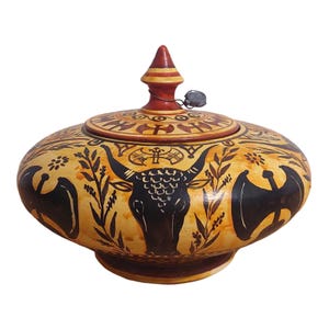 May include: A ceramic jar with a lid, decorated with a black bull, stylized axes, and floral motifs. The jar is painted in shades of yellow, orange, and black.