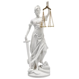 Puede incluir: Una estatua blanca de la Dama de la Justicia con los ojos vendados, sosteniendo una balanza de metal dorado en la mano izquierda y una espada en la derecha. La figura se apoya en una base circular con una serpiente enroscada en un libro.