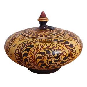 Puede incluir: Un tarro decorativo con tapa, base de color beige claro y intrincados patrones florales de color marrón oscuro. La tapa está rematada con un pináculo rojo oscuro y marrón. El tarro tiene forma redondeada y probablemente se utiliza para el almacenamiento.
