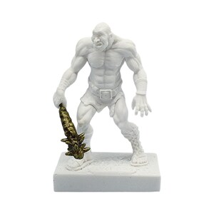May include: A white figurine of a muscular humanoid figure holding a gold-colored club. The figure is standing on a white rectangular base. The figurine has a stern expression and is wearing a loincloth and armbands.