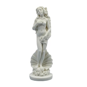 Può includere: Una statua bianca di una donna in piedi su una conchiglia. La statua ha lunghi capelli fluenti ed è parzialmente drappeggiata. La scultura è su una base rotonda.