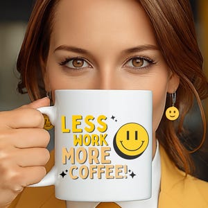 May include: White coffee mug with the text "LESS WORK MORE COFFEE!" in yellow and orange. A yellow smiley face is on the right side of the mug. The person in the image is wearing a yellow blazer and has a pair of smiley face earrings.