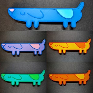 May include: Five dachshund-shaped dog figurines in different colors. The figurines are blue, purple, yellow, green, and orange. Each figurine has a simple, cartoon-like design.