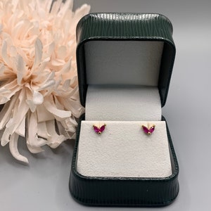 Può includere: Un paio di orecchini d'oro con piccoli accenti di pietre preziose rosse in una scatola per gioielli verde.