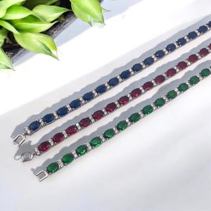 May include: Three silver bracelets with oval-shaped gemstones. The bracelets feature blue, red, and green gemstones.