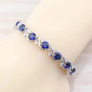 Puede incluir: Una pulsera de plata con un diseño delicado que presenta piedras redondas azules y blancas alternadas. La pulsera tiene un aspecto delicado y femenino.