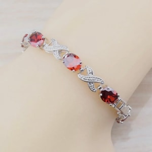May include: A silver bracelet with red oval-shaped gemstones and a criss-cross design.