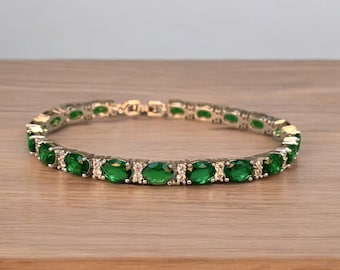 May include: A silver tennis bracelet with oval-shaped green gemstones and smaller clear gemstones.
