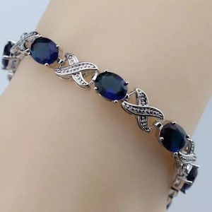 May include: A silver bracelet with a delicate design featuring alternating oval-shaped blue gemstones and silver accents.