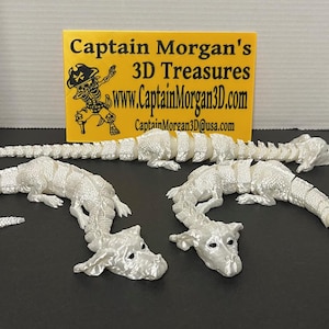 May include: Three white plastic dragon figurines with segmented bodies. The dragons are posed in a variety of positions, with their heads and tails raised. The figurines are made by Captain Morgan's 3D Treasures.