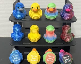 May include: A set of 10 rubber duckies on a black tiered display stand. The ducks are crocheted and come in a variety of colors, including blue, yellow, green, and purple. The ducks have the text "You've Been Ducked" on the bottom.