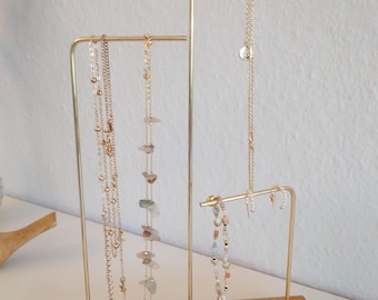 May include: A gold metal jewelry stand with a wooden base. The stand has three bars for hanging necklaces and a horizontal bar for bracelets or earrings.