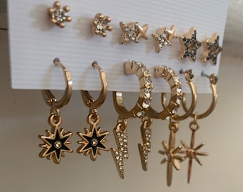 May include: A set of gold-tone earrings with various star and lightning bolt designs. Some earrings are stud earrings, while others are hoop earrings with dangling charms.