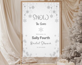 May include: A white sign with a gold frame and snowflakes printed on it. The sign reads "Snow In Love" and "Welcome to Sally Fourth Bridal Shower 12.20.2025".