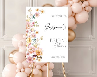 Può includere: Un cartello bianco con illustrazioni floreali sul lato sinistro e testo che recita "Benvenuti al Bridal Shower di Jessica il 25 aprile 2024". Il cartello è appoggiato su un cavalletto dorato.