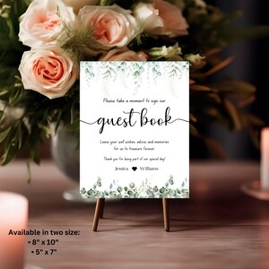 May include: A white sign with green foliage border and text that reads "Please take a moment to sign our guest book. Leave your well wishes, advice, and memories for us to treasure forever. Thank you for being part of our special day! Jessica  Williams". The sign is available in two sizes: 8" x 10" and 5" x 7".